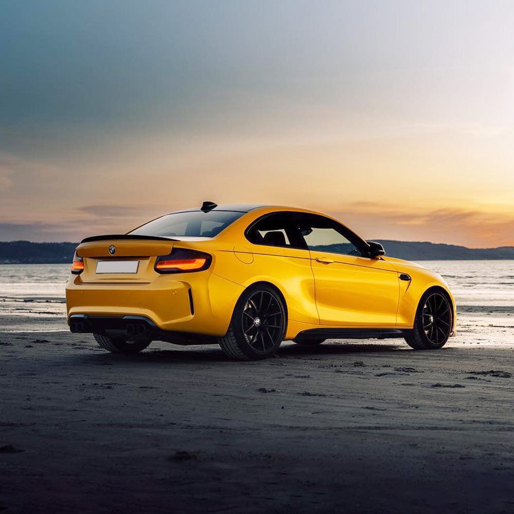 Rear angle of a BMW coupe wrapped in Golden Yellow (RB25-HD) gloss vinyl, perfectly complementing the beachside sunset.