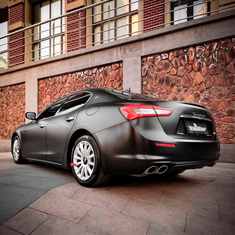 Luxury sedan fully wrapped in TeckWrap Black Matte Vinyl parked outdoors, emphasizing the wrap's