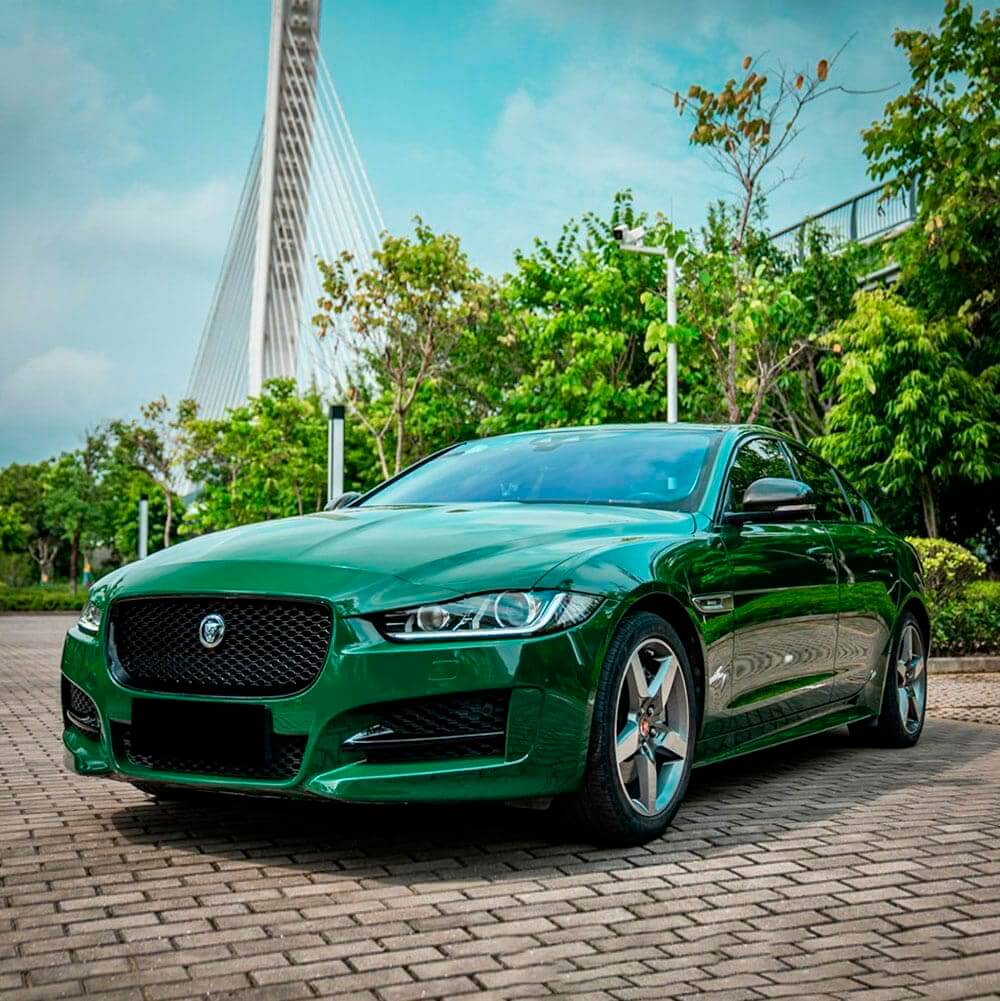 A Jaguar XE sedan customized with a vibrant high-gloss green vinyl wrap