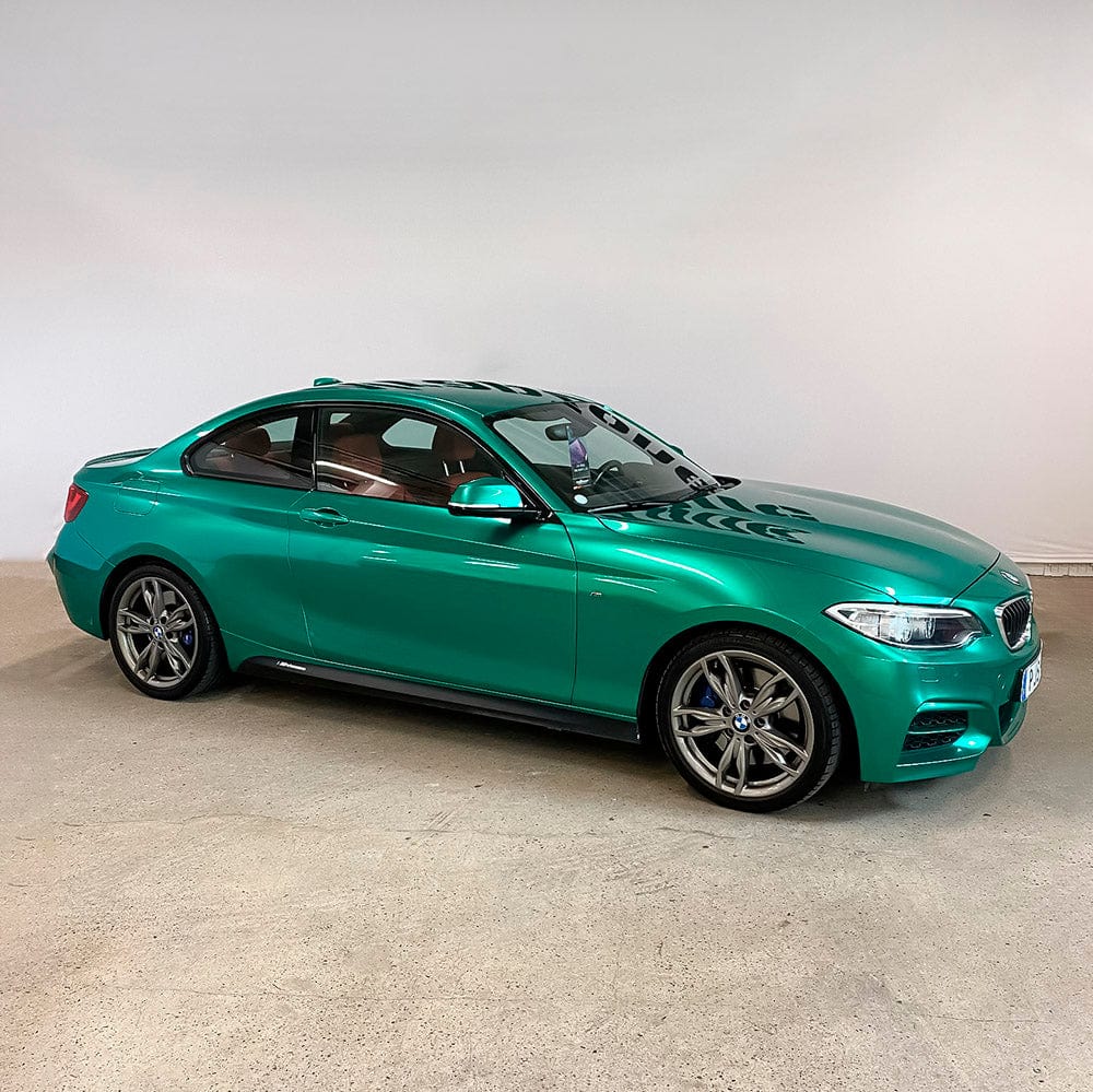 Side view of a BMW wrapped with TeckWrap Ocean Green Gloss Vinyl, illustrating its captivating turquoise hue and sleek glossy appearance.